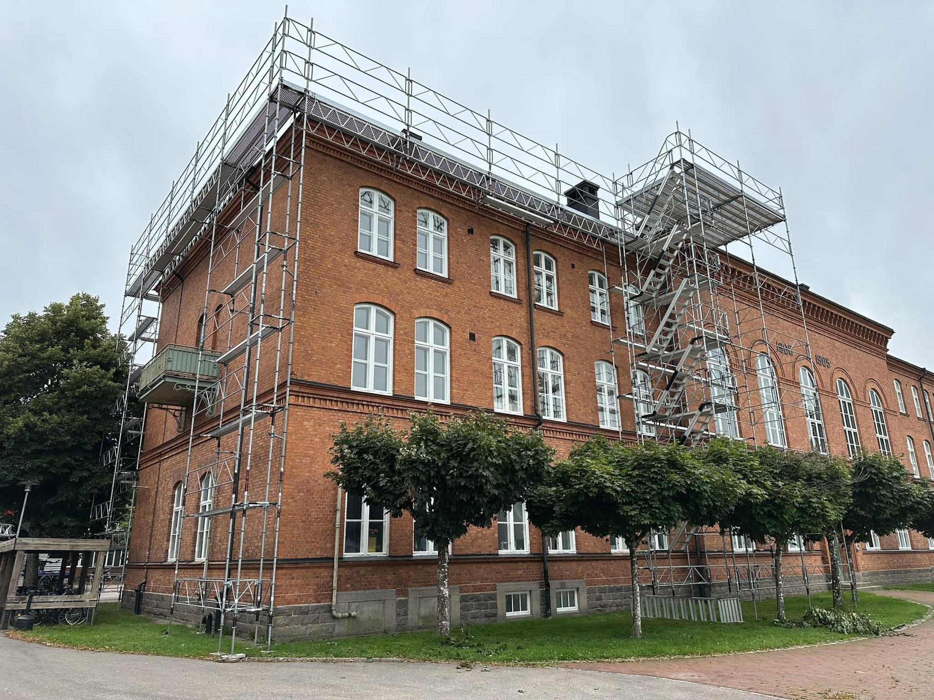 Fasadställning med trapptorn och takfotsskydd runt en stor tegelbyggnad