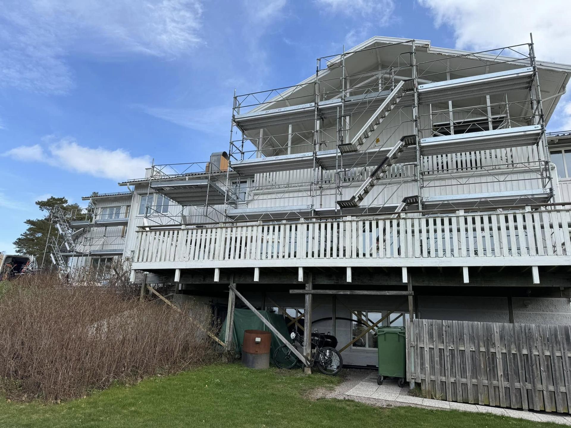 Ställning med trappor runt ett vitt trähus vid fasadrenovering