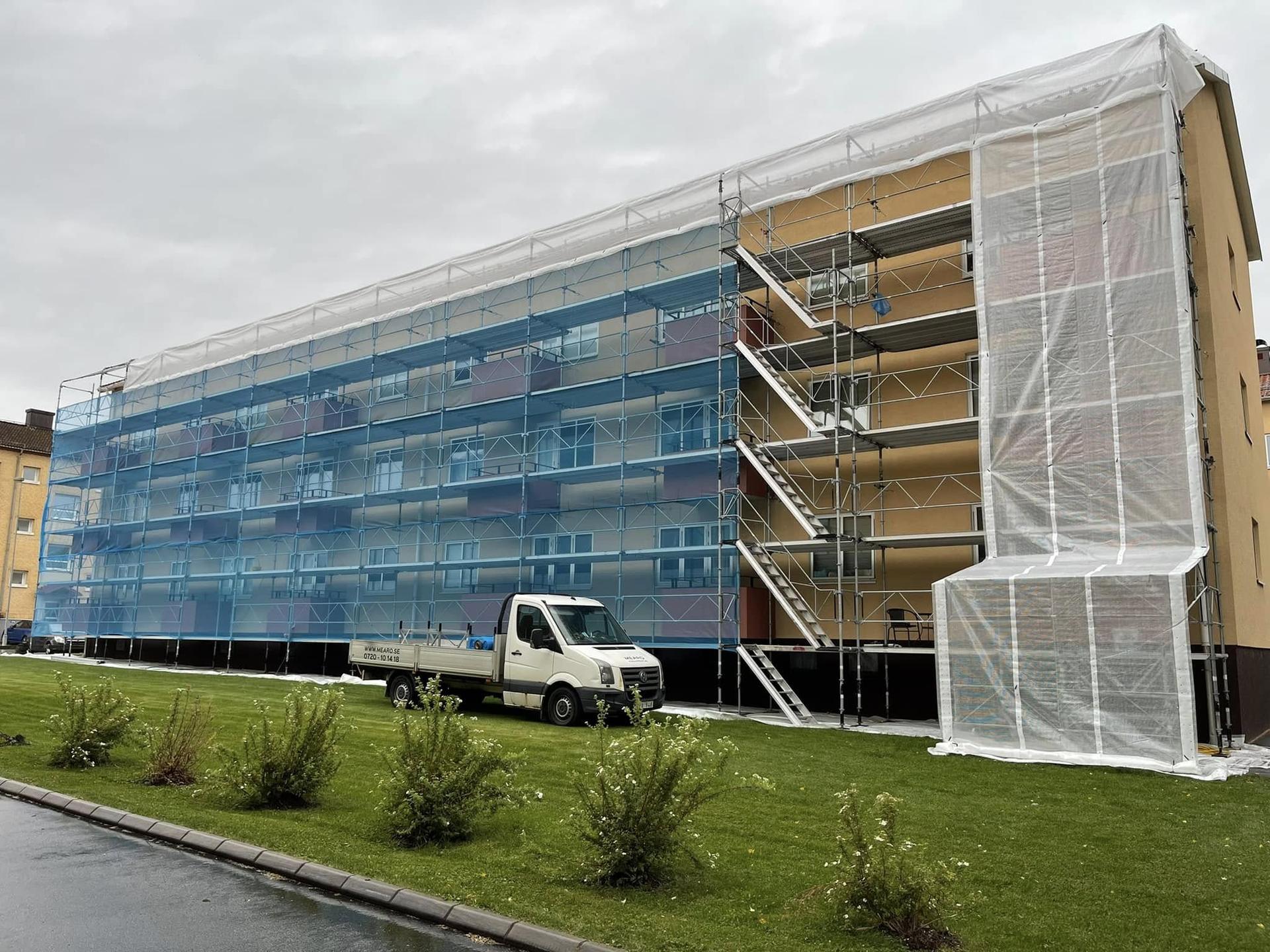 Nätklädd fasadställning med väderskyddstak på ett långt flerbostadshus